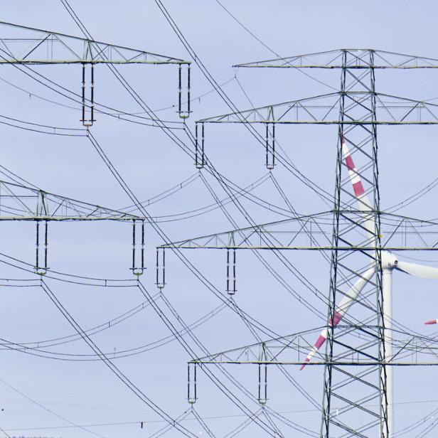 Mehrere Strommasten und Windräder vor einem hellblauen Himmel.
