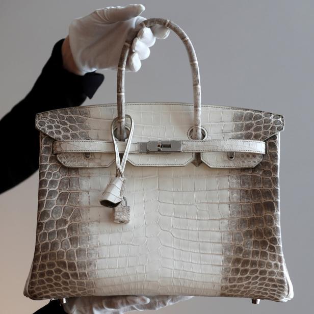 Eine weiße Hermès Birkin Bag aus Krokodilleder wird von einer Person mit weißen Handschuhen gehalten.