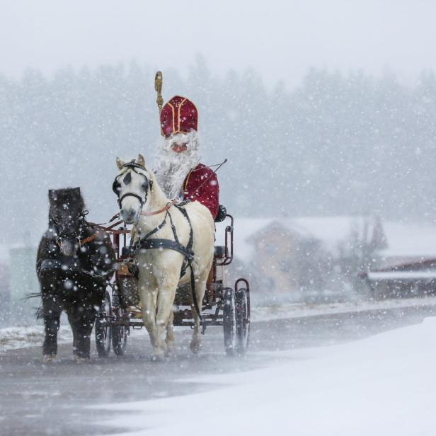 Der Nikolaus fährt mit einer Kutsche, gezogen von zwei Pferden, durch den Schnee.