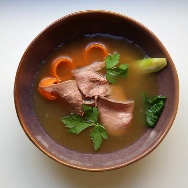 Eine Schüssel mit Rindfleischsuppe, garniert mit Karotten und Petersilie.