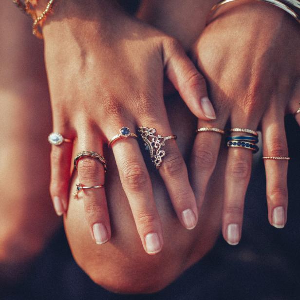 Die Hände einer Person sind mit mehreren goldenen Ringen und Armbändern geschmückt.