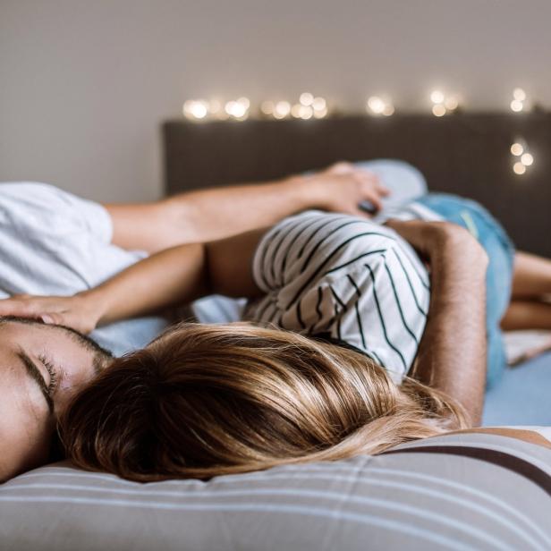 Ein Paar liegt eng umschlungen im Bett, mit Lichterkette im Hintergrund.