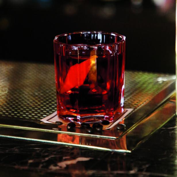 Ein roter Cocktail mit einer Orangenzeste steht auf einer Bar.