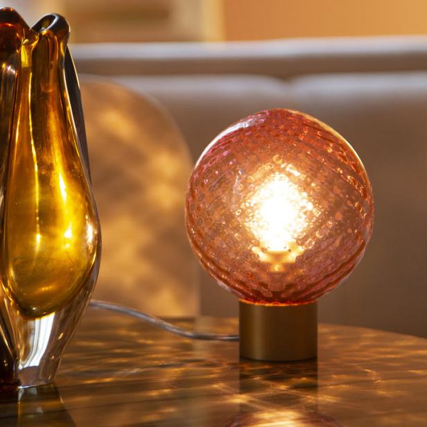 Eine orangefarbene Kugel-Lampe steht neben einer Vase auf einem Tisch.
