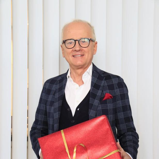 Ein Mann im Anzug hält ein rot verpacktes Geschenk mit goldener Schleife.