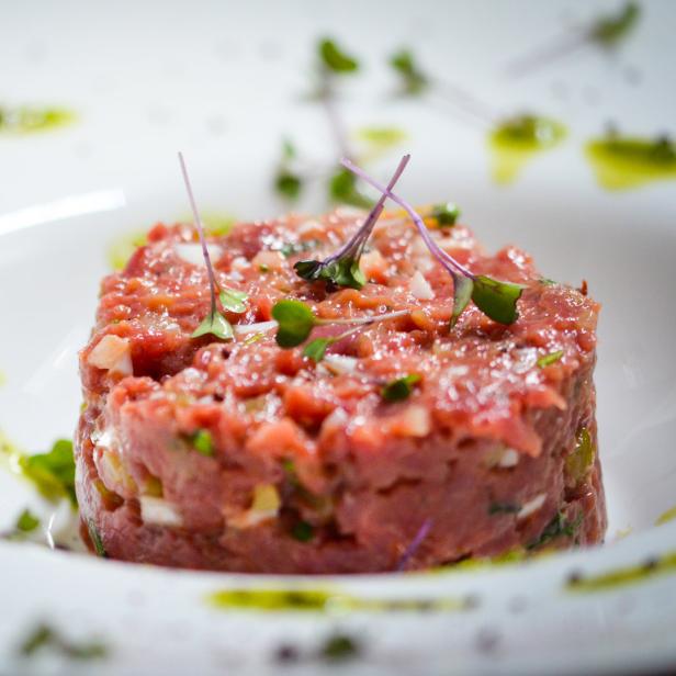 Ein quadratisches Beef Tatar auf einem weißen Teller, garniert mit Kräutern.