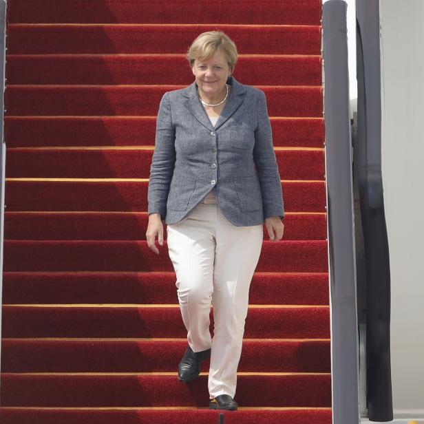 Angela Merkel geht eine mit rotem Teppich ausgelegte Flugzeugtreppe hinunter.