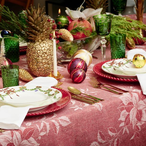 Ein festlich gedeckter Tisch mit goldenen Ananas, Weihnachtskugeln und rotem Blumendekor.