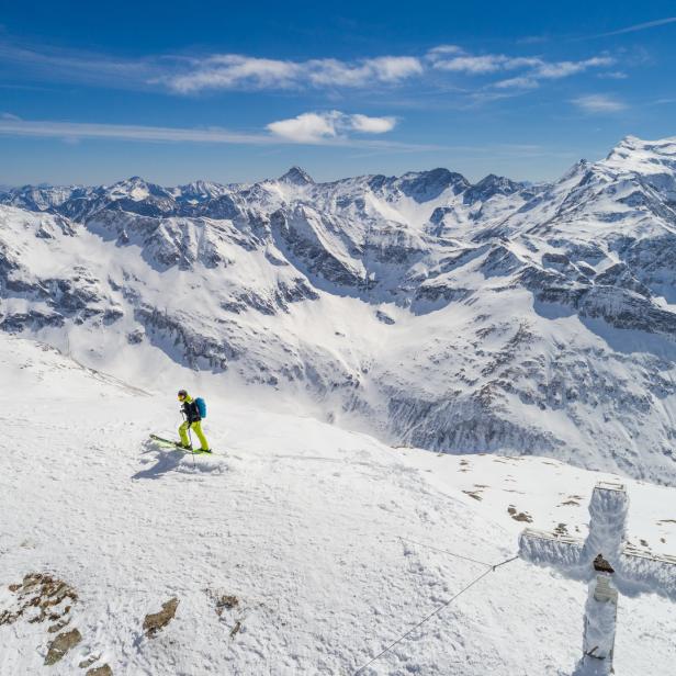 Ein Skifahrer fährt auf einem schneebedeckten Berg in der Nähe eines Gipfelkreuzes.