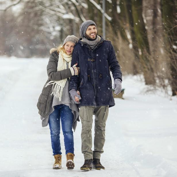 Ein Paar spaziert Hand in Hand durch eine verschneite Winterlandschaft.
