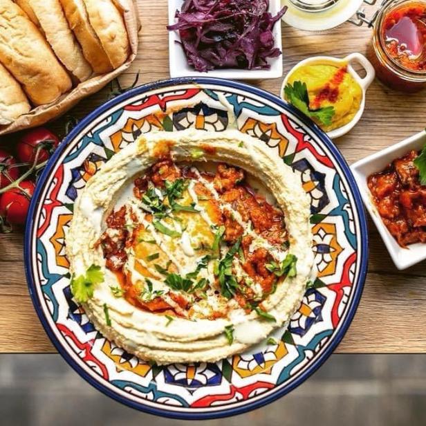 Ein Teller Hummus mit Toppings, serviert mit Brot, Tomaten und verschiedenen Dips.