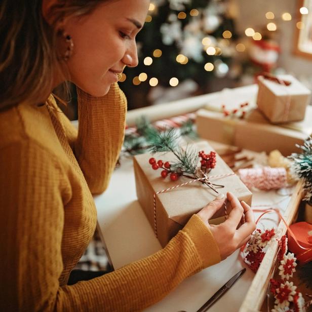 Eine Frau verpackt Weihnachtsgeschenke mit Tannenzweigen und roten Beeren.