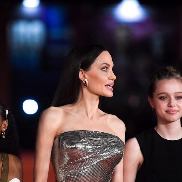 Angelina Jolie mit zwei jungen Frauen auf einem roten Teppich.