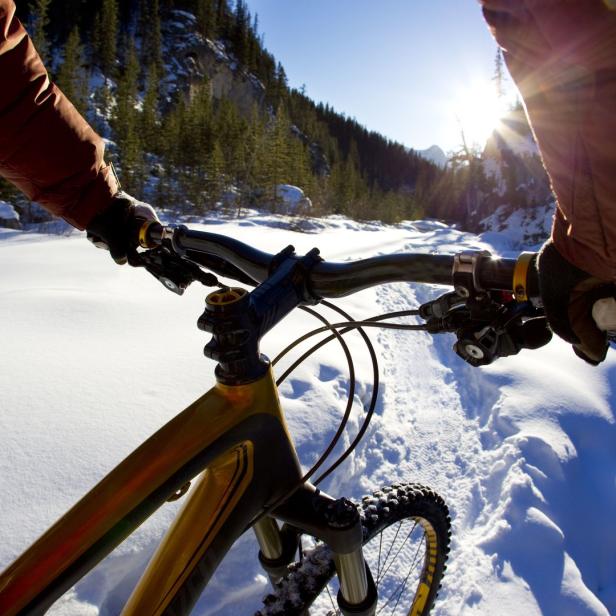 Ein Mountainbike fährt auf einem verschneiten Weg entlang eines Flusses.