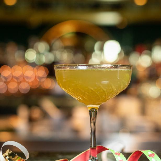Ein Cocktail in einem eleganten Glas, dekoriert mit einer Schleife und kleinen Figuren.