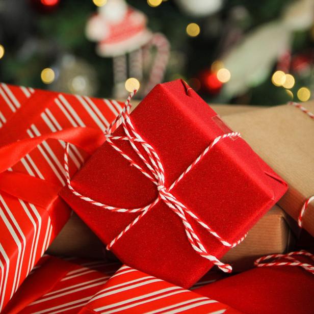 Mehrere rot und braun verpackte Weihnachtsgeschenke liegen vor einem Weihnachtsbaum.
