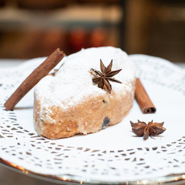 Ein Stollen mit Puderzucker, Zimtstangen und Sternanis auf einer Tortenplatte.