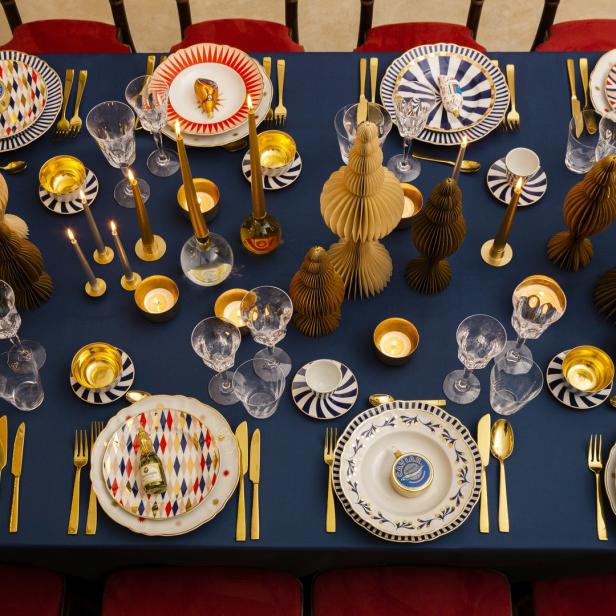 Ein festlich gedeckter Tisch mit goldenem Besteck, Kerzen und Dekorationen auf blauem Grund.