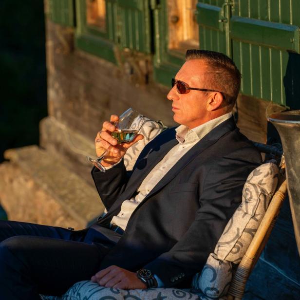 Ein Mann mit Sonnenbrille sitzt draußen und genießt ein Glas Wein.