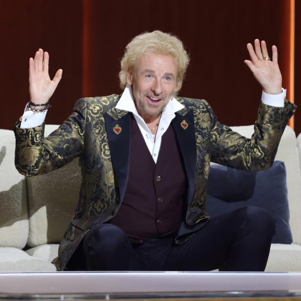 Thomas Gottschalk sitzt auf einer Couch und gestikuliert mit den Händen.