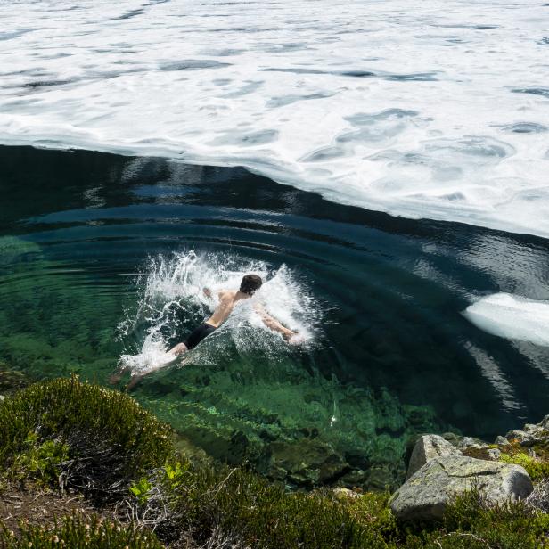 Ein Mann springt in einen Bergsee mit teilweise geschmolzenem Eis.