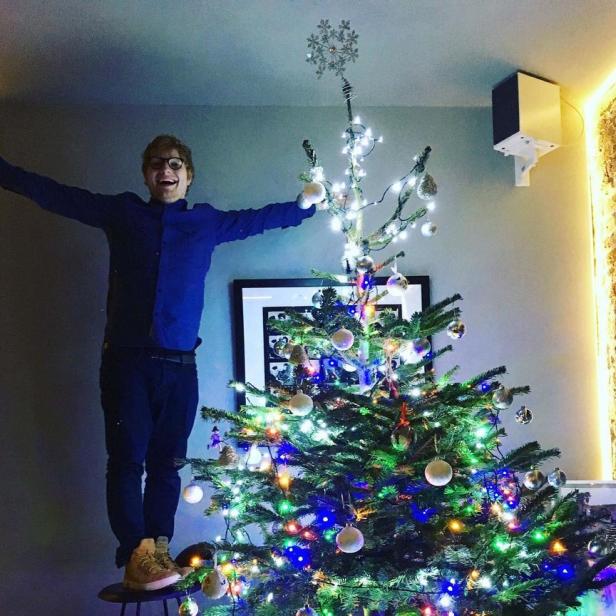 Ein Mann steht auf einem Hocker und schmückt einen Weihnachtsbaum mit bunten Lichtern.