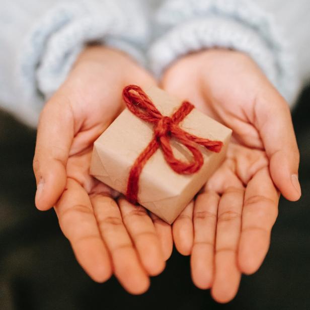 Ein kleines Geschenk mit roter Schleife liegt in den Händen einer Person.