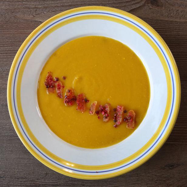 Ein Teller Kürbissuppe, garniert mit Croutons und rosa Pfefferbeeren.