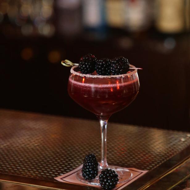 Ein Brombeer-Cocktail mit Zuckerrand steht auf einer Bar.