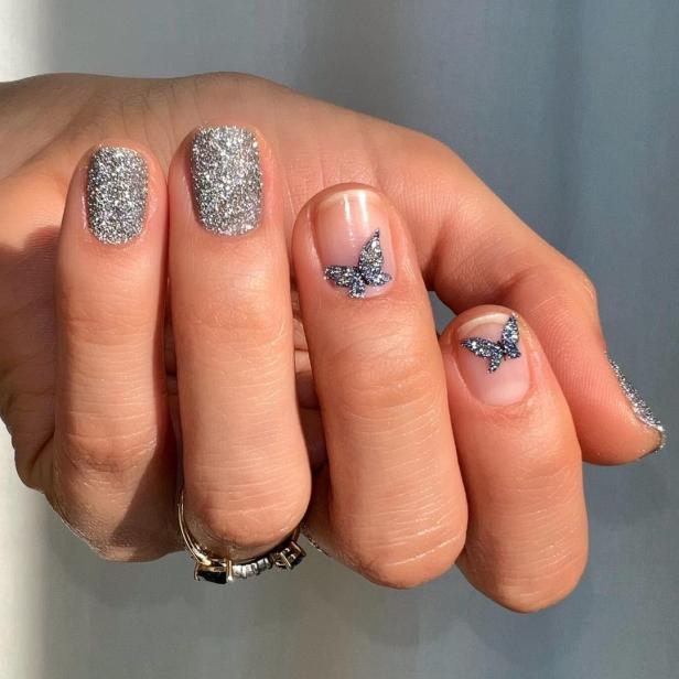 Nahaufnahme einer Hand mit silbernem Glitzerlack und Schmetterlingsmotiven.