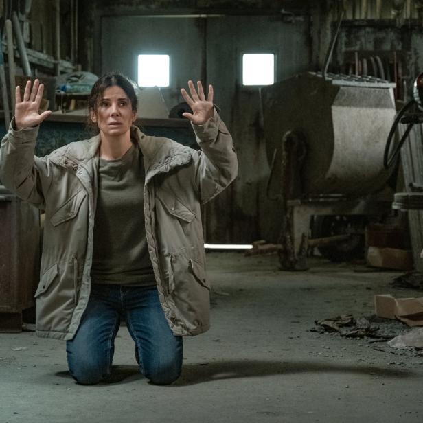 Sandra Bullock kniet mit erhobenen Händen in einer Lagerhalle.