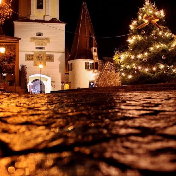 Ein beleuchteter Weihnachtsbaum steht vor einem historischen Gebäude in der Nacht.