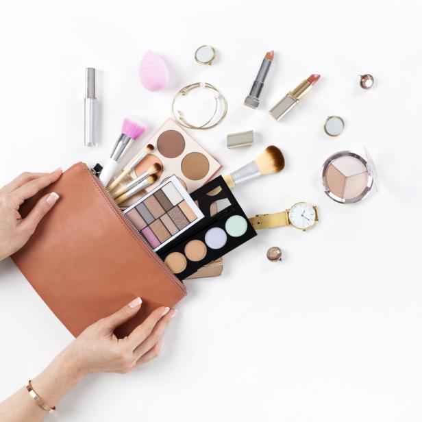 Eine Kosmetiktasche wird von Händen gehalten, umgeben von Make-up-Produkten und Accessoires auf einem weißen Hintergrund.