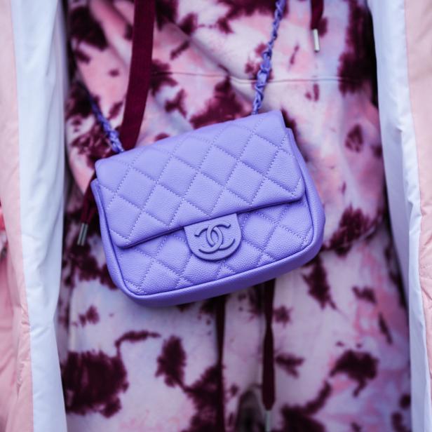 Eine lila Chanel-Tasche hängt vor einem rosa-lila gefärbten Hoodie und einer rosa Jacke.