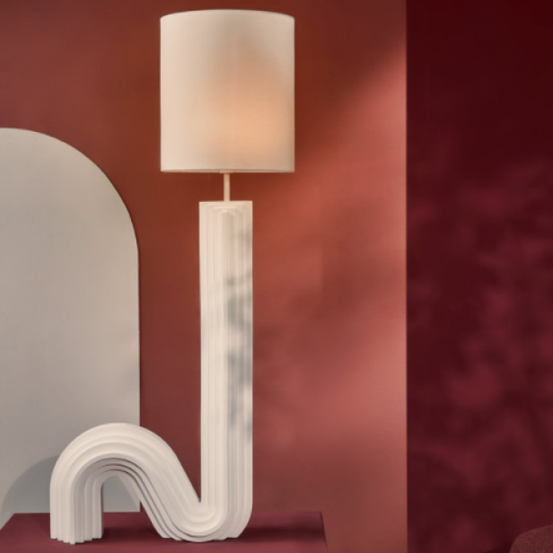 Eine moderne Stehlampe mit einem gewundenen, weißen Sockel und einem Lampenschirm steht in einem Raum.