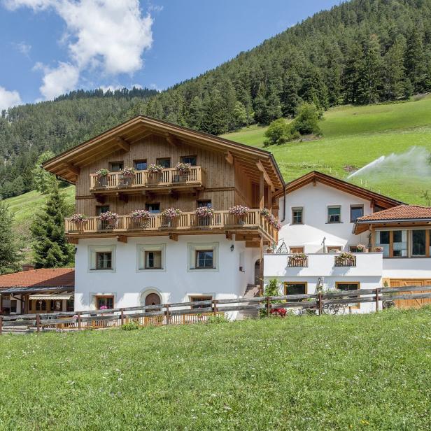 Ein traditionelles Bauernhaus mit blumengeschmückten Balkonen vor einer grünen Berglandschaft.