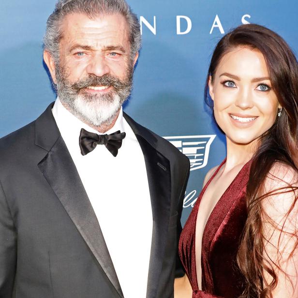 Mel Gibson posiert mit einer jungen Frau auf einer Veranstaltung.