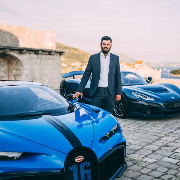 Ein Mann im Anzug posiert zwischen einem blauen Bugatti und einem Rimac Nevera.
