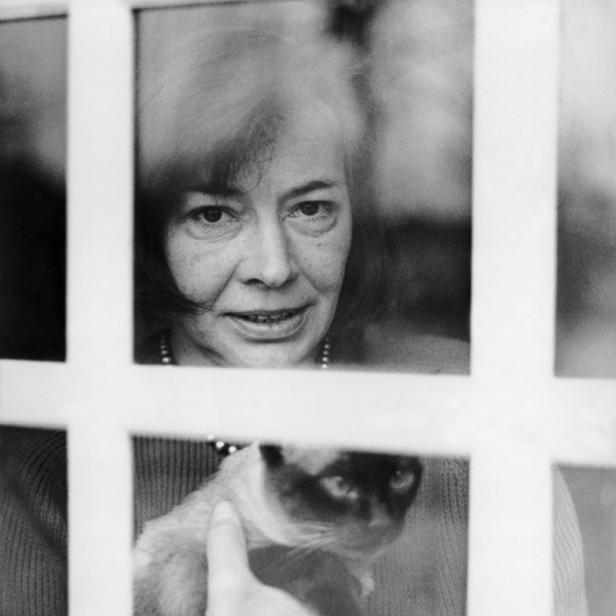 Eine Frau hält eine Siamkatze hinter einem Fenster.