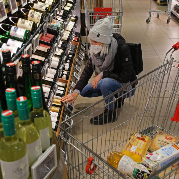 Eine Frau mit Maske kauert vor einem Weinregal in einem Supermarkt.
