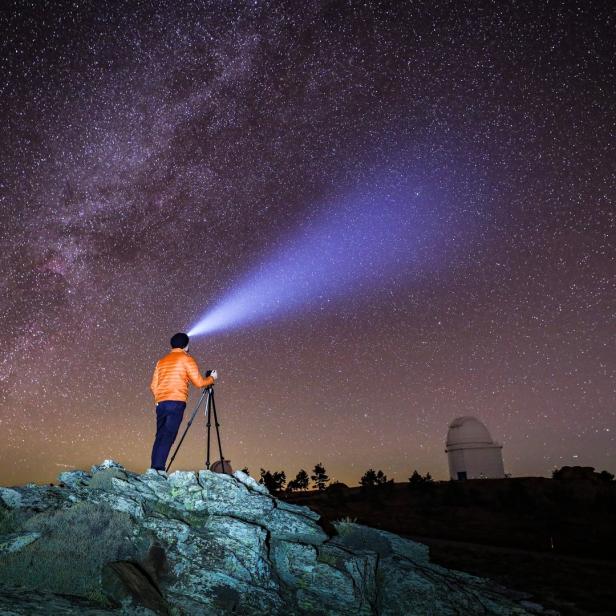 Ein Mann fotografiert mit Stativ und Stirnlampe den Sternenhimmel.