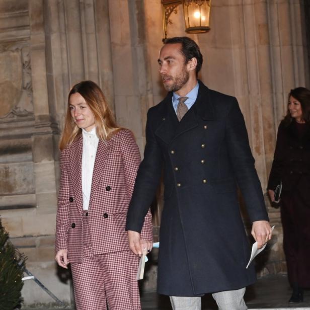 James Middleton und Ehefrau Alizée Thevenet, sie in einem karierten Hosenanzug, er in einem Mantel, gehen Hand in Hand.