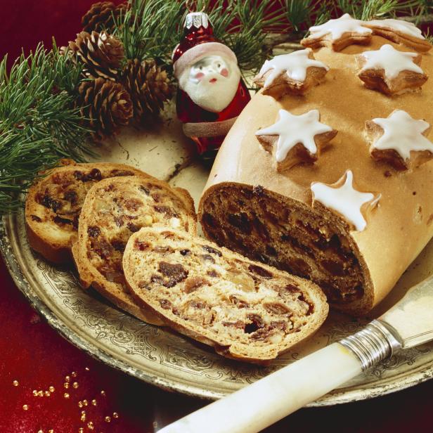 Ein angeschnittener Weihnachtsstollen mit Zimtsternen und einem Weihnachtsmann auf einem Teller.