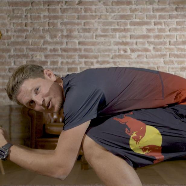 Ein Mann in Sportkleidung kauert vor einer Ziegelwand.