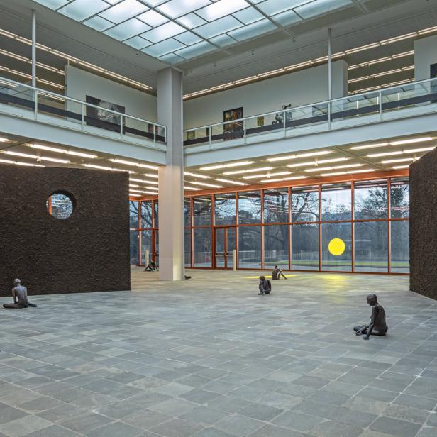 In einem Ausstellungsraum sitzen mehrere dunkle Statuen auf dem Boden.