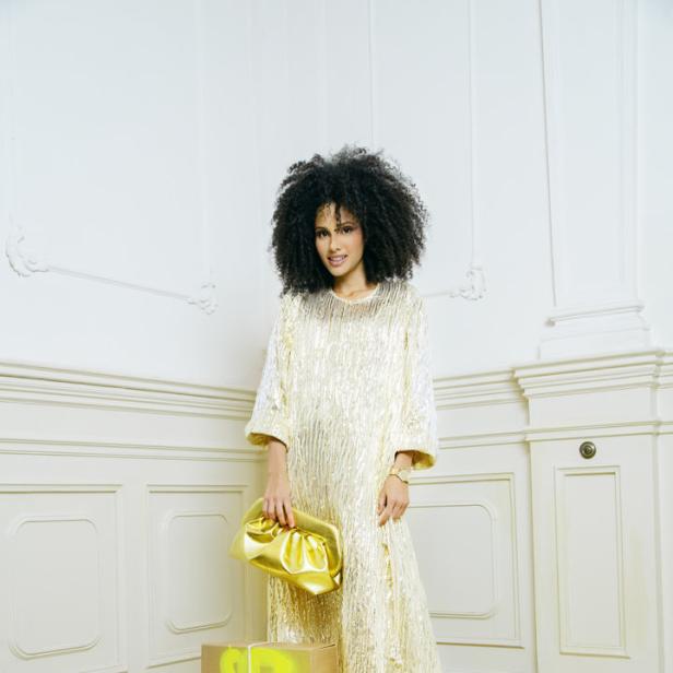Eine Frau in einem goldenen Kleid mit einer goldenen Handtasche und einem Paket.