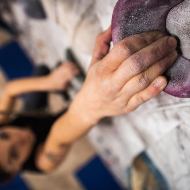 Die Hand einer Kletterin greift nach einem lila Klettergriff.