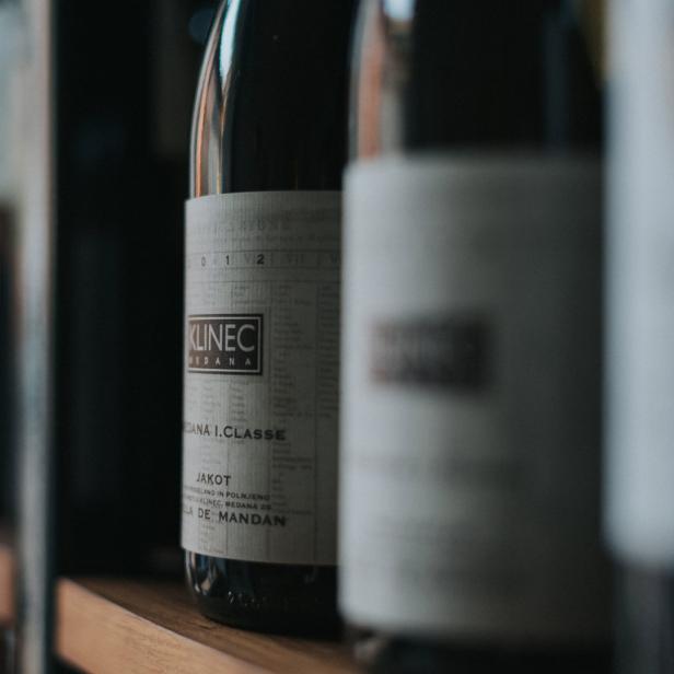 Mehrere Flaschen Klinec Medana Wein stehen auf einem Holzregal.