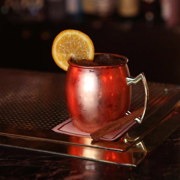 Ein Moscow Mule in einem Kupferbecher mit einer Orangenscheibe und einer Zimtstange an einer Bar.