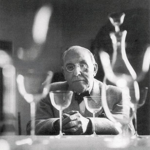 Der Fotograf Man Ray hinter einer Reihe von Gläsern und einer Karaffe.